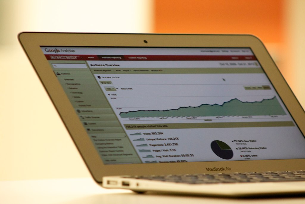 Close-up of a laptop screen showing an analytics dashboard with an upward-trending performance line graph, visitor stats, and a pie chart, shallow depth of field